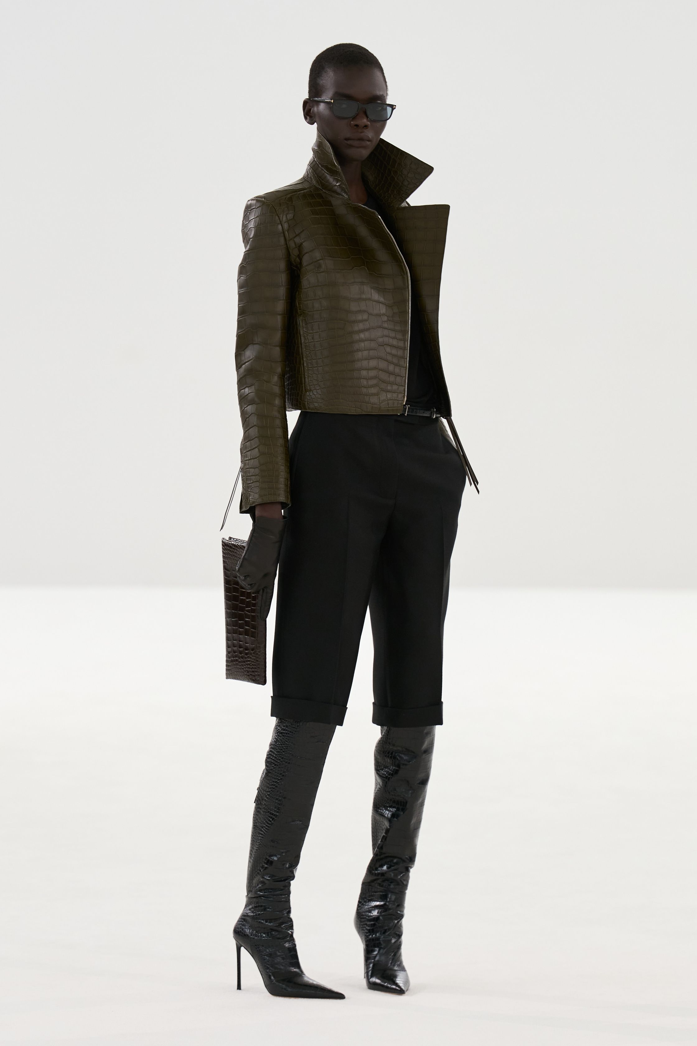 Tom Ford 2026秋冬系列回归品牌标志性的性感极简主义。高腰铅笔裙、透明材质层叠与利落西装展现强烈的都市魅力。黑色、棕色与金属光泽构成成熟而冷峻的色彩体系，皮革与光泽面料的运用强化性感张力。整体造型强调身体线条与权力感，展现Tom Ford一贯的夜晚都市美学-顽石频道趋势研究